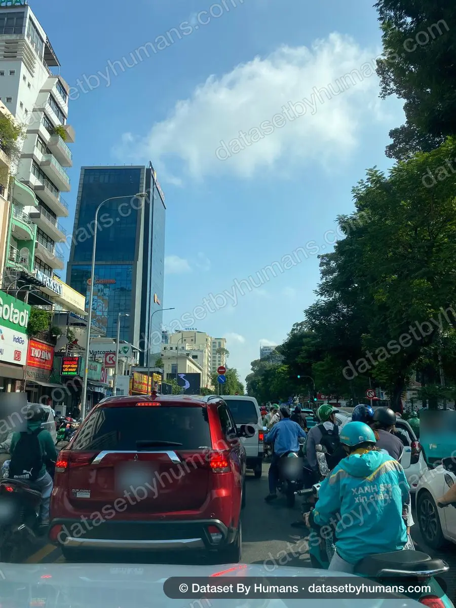 Dense morning traffic in a busy city centre: motorbikes and an SUV waiting at a junction between office towers