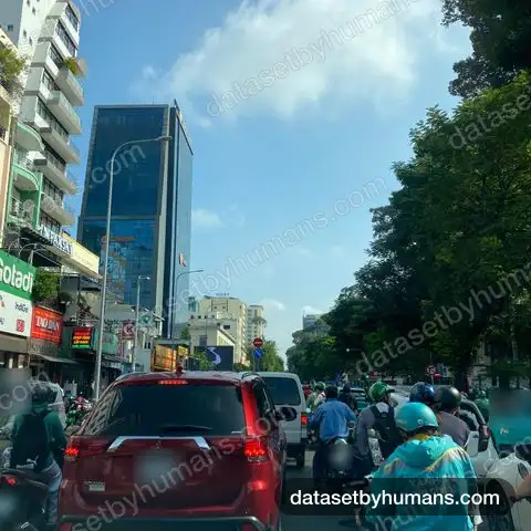 Dense morning traffic in central Ho Chi Minh City: motorbikes and an SUV waiting at a junction between office towers