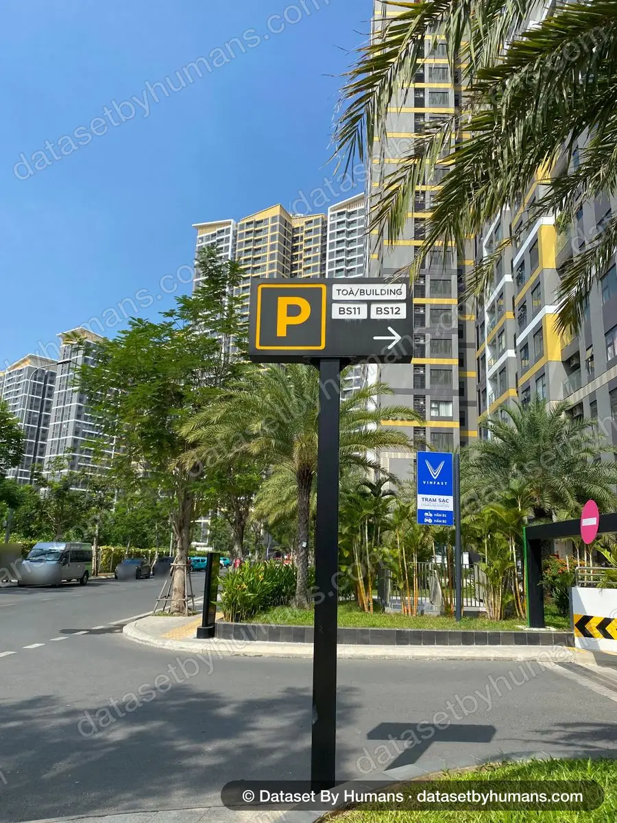 Bilingual parking sign reading 'Toà/Building BS11 BS12' with an EV charging station sign, in front of high-rise apartments