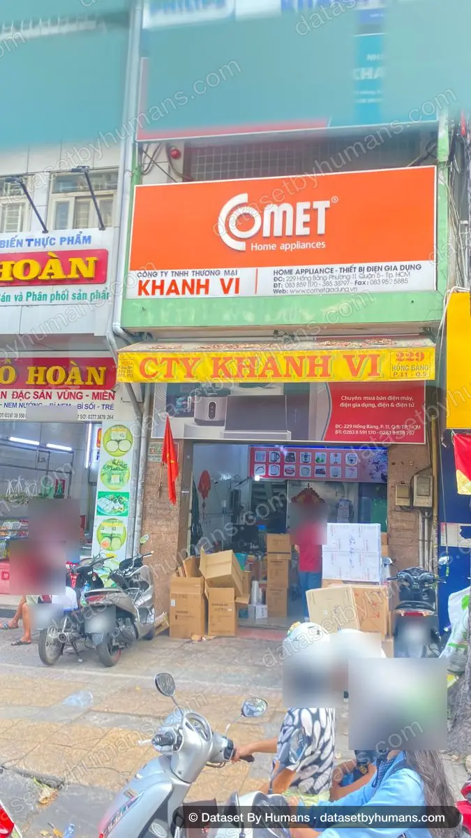 Shopfront of a home-appliance company with dense Vietnamese signage, neighbouring food shop signs and motorbikes on the pavement