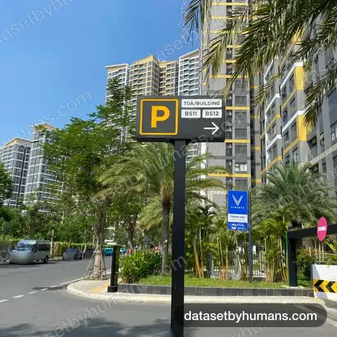 Bilingual parking sign reading 'Toà/Building BS11 BS12' with an EV charging station sign, in front of high-rise apartments